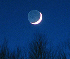 光っていない部分もうっすらと白く見える月。全体の形は満月と同じまん丸。