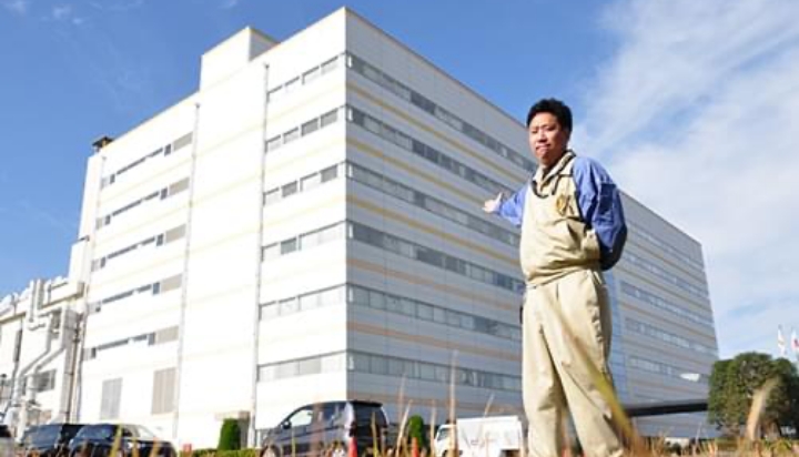 熊谷製作所の7号館建屋外観と案内する男性